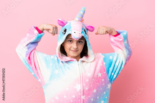 Little caucasian woman wearing a unicorn pajama isolated on pink background doing strong gesture
