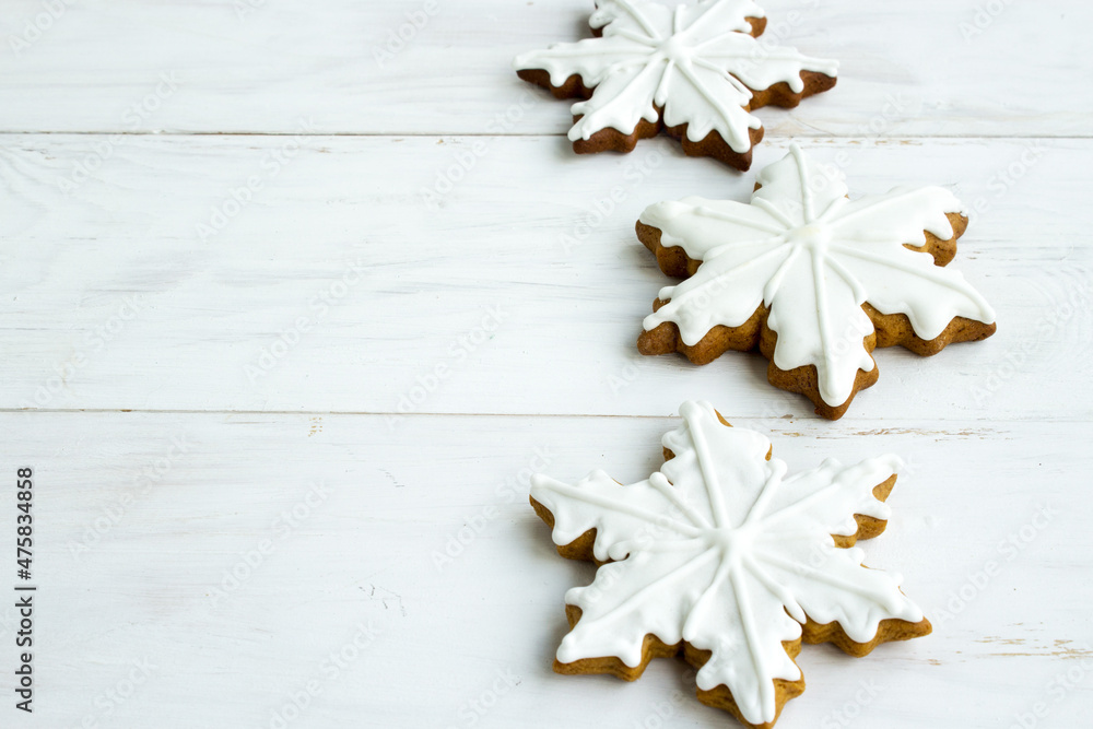 Fototapeta premium Christmas gingerbread. Edible Christmas decor concept. Gingerbread cookies in white glaze on a light wooden background. Christmas traditions. Copy space.