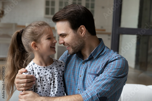 Close up loving smiling father hugging laughing little daughter at home, family enjoying tender moment, having fun at home together, caring young Caucasian dad and girl child looking in eyes