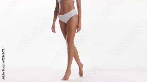 Medium long shot of African American good-looking slim woman in white underwear makes a step to the camera on tiptoes on white background | Smooth legs concept photo