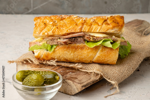 Cuban sandwich with pork and pickles on a serving board, light table.