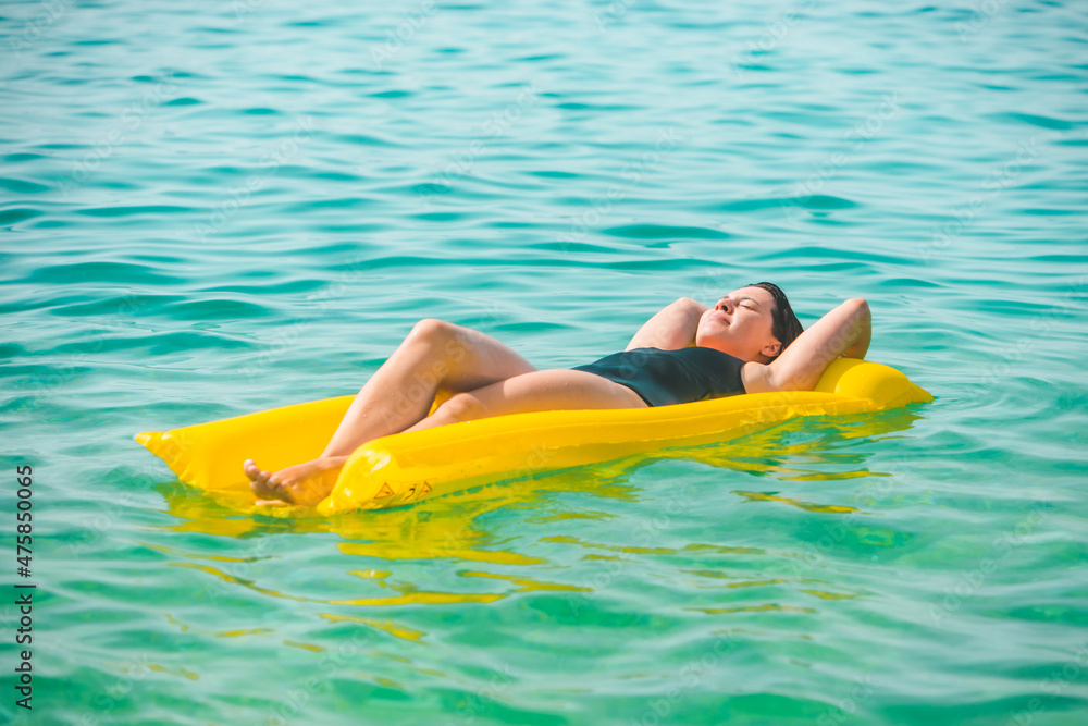 beautiful sexy woman laying on yellow inflatable mattress at sea water