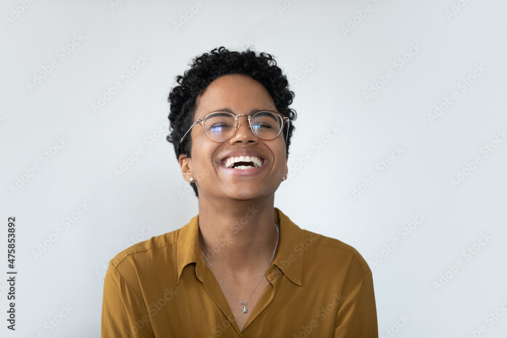 Obraz premium Overjoyed millennial African American woman in eyeglasses laughing, showing positive emotions near white wall. Happy female client demonstrating perfect whitening smile, isolated on studio wall.