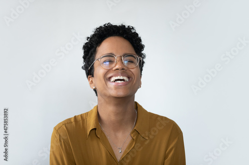 Overjoyed millennial African American woman in eyeglasses laughing, showing positive emotions near white wall. Happy female client demonstrating perfect whitening smile, isolated on studio wall. © fizkes