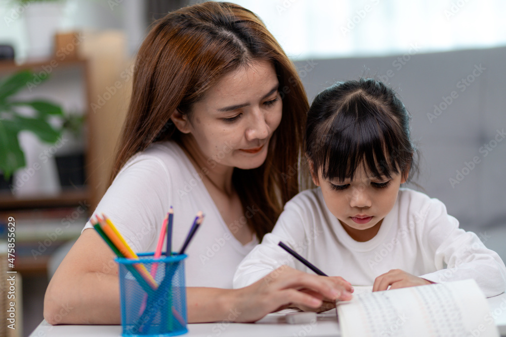 Obraz premium Beautiful Asian woman helping her daughter with homework at home.