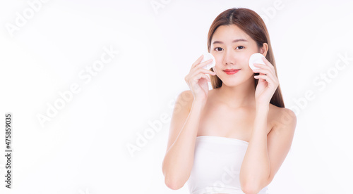 Asian woman using cotton pad cleansing makeup on face sitting over isolated white background. Asian girl holding cotton wool with lotion remove makeup skin face. Cosmetology treatment cleanser concept