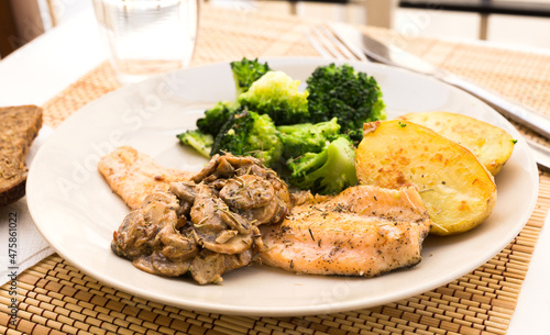 fried river trout fillet with a complex side dish of broccoli, baked potatoes and mushroom sauce