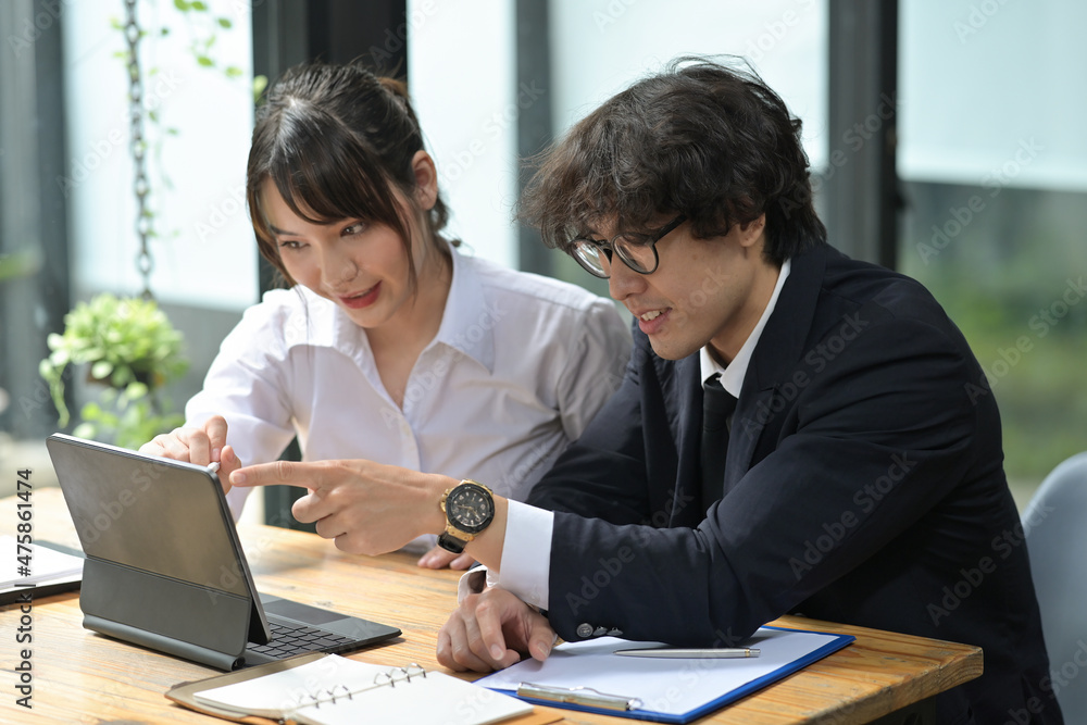Photo of young businesspeople working together at the wooden working desk with a digital tablet and clipboard. Photo of young businesspeople working together at the wooden working desk with a digital tablet and clipboard.