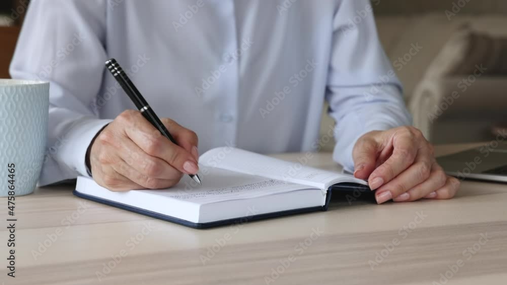 Taking notes. Close up view of older businesswoman writing work information on open page of business daybook by hand. Mature woman entrepreneur planning day handwriting list of tasks to daily planner Taking notes. Close up view of older businesswoman writing work information on open page of business daybook by hand. Mature woman entrepreneur planning day handwriting list of tasks to daily planner