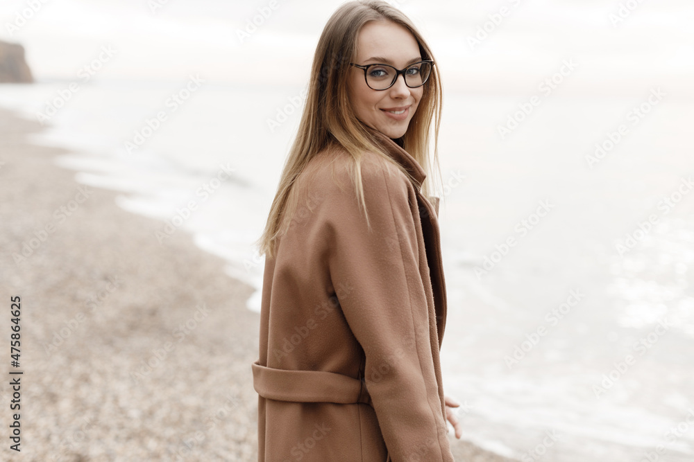 portrait of a young happy woman in coat and glasses outdoor on the beach autumn spring portrait of a young happy woman in coat and glasses outdoor on the beach autumn spring