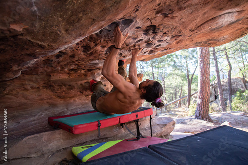 From below back view of young sportsman with naked torso climbing natural rocky roof 