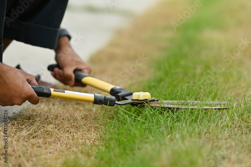 Cropped image of gardener's hand using lawn scissors on the grass field.