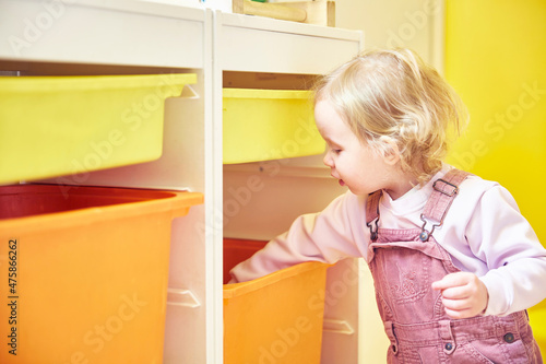 little girl takes out or lays out toys from the drawer of the rack.