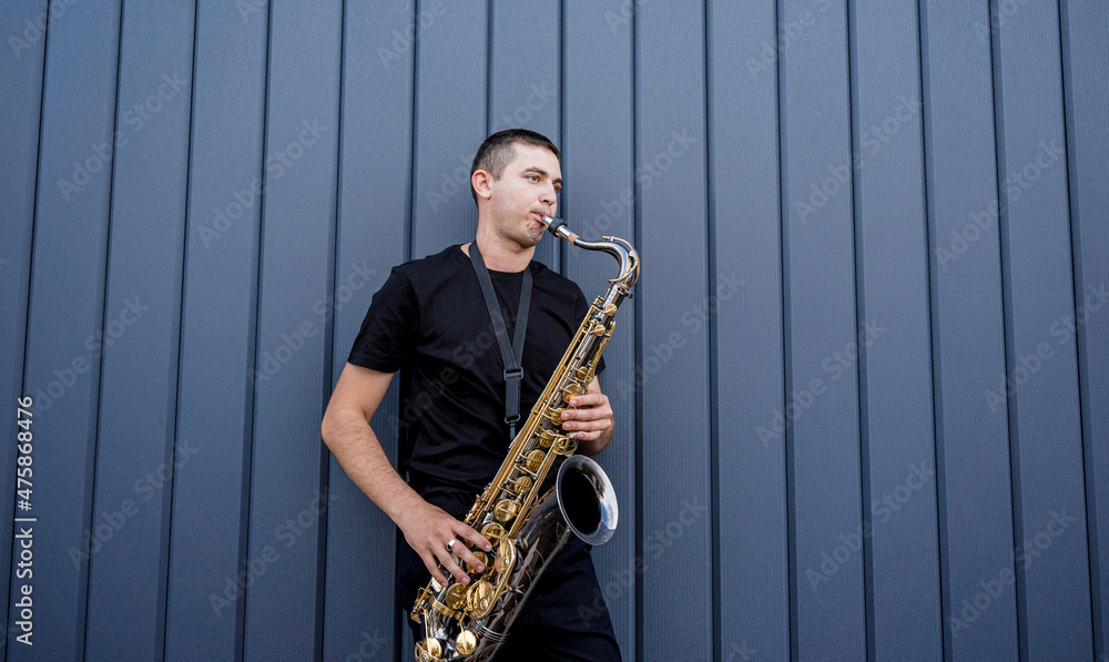 Fototapeta premium Young street musician playing saxophone near the big blue wall