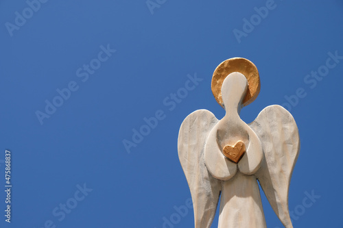 Wooden angel with golden halo and heart in hands. Blue sky background. photo