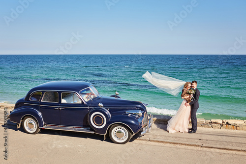beautiful young wedding couple hugging near the car on the beach