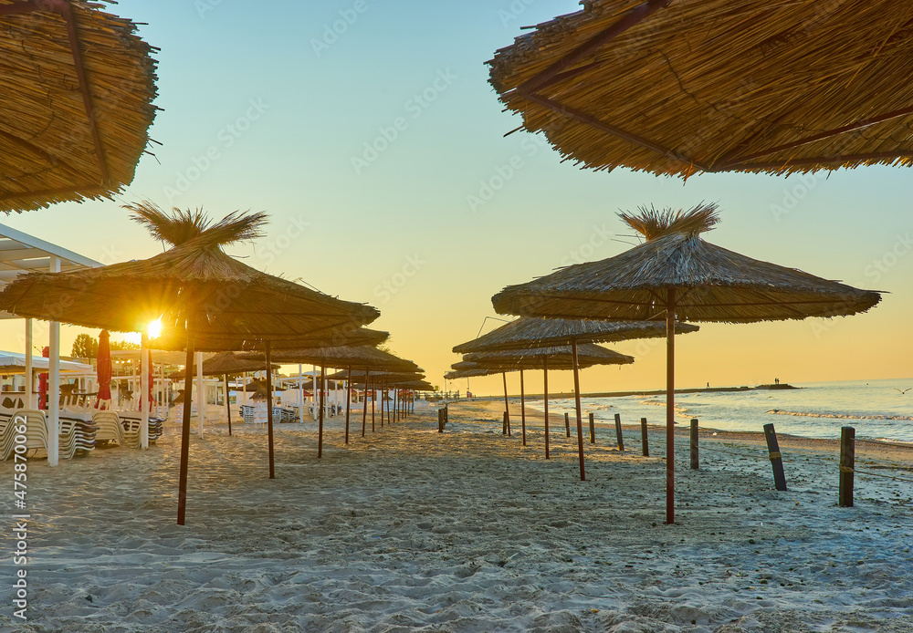 Seashore, sand beach with umbrellas and sunbeds on background of the sea and sky