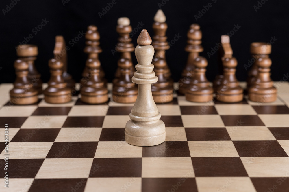 A lone white chess king stands on the chessboard opposite the opponent's chess pieces. The concept of the courage of a leader challenging an opponent. One warrior in the field. One against the enemy. A lone white chess king stands on the chessboard opposite the opponent's chess pieces. The concept of the courage of a leader challenging an opponent. One warrior in the field. One against the enemy.