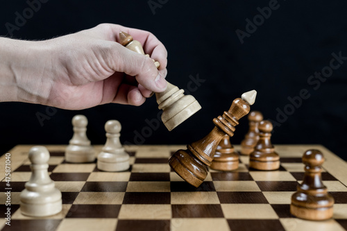 A close-up of a man's hand puts a checkmate in a chess board game. The male hand moves the white king to defeat the black king. A game of chess. Management and leadership concept
