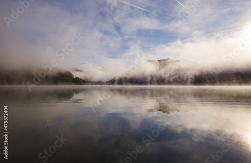 Alpiner Stausee Sylvensteinspeicher im morgendlichen Nebel und Kondensstreifen an einem kalten Tag im Herbst 