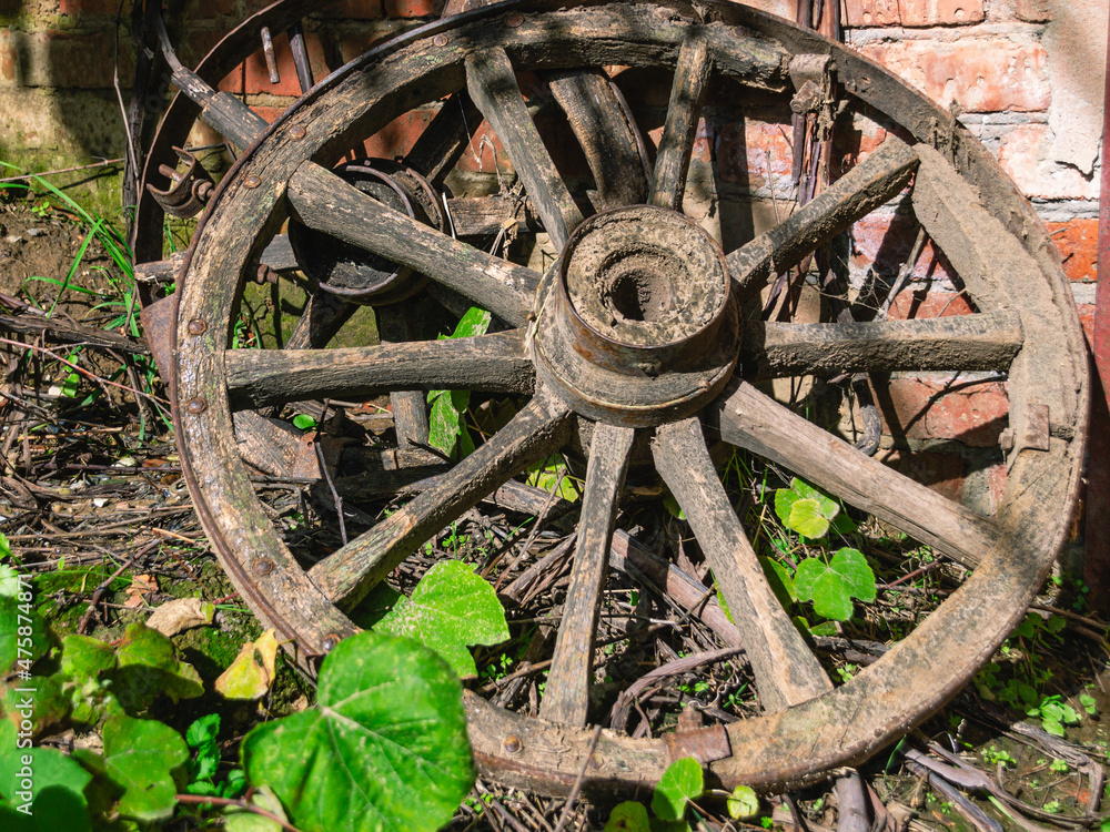 An old wooden cart wheel is lying on the ground. A wooden cart wheel under the sun near a barn in the village An old wooden cart wheel is lying on the ground. A wooden cart wheel under the sun near a barn in the village