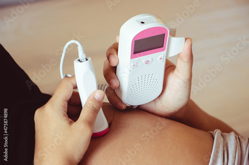 Photographie The close up pregnant woman using pocket fetal doppler to monitor baby heart beat