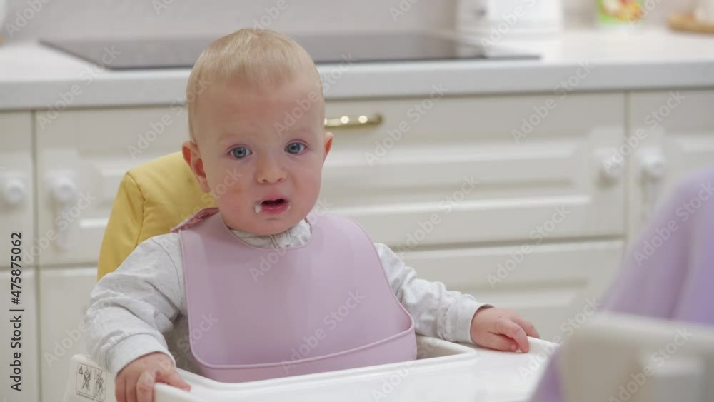Mother feeding her baby with porridge, hungry baby boy knocking on the table with his hand impatiently. 9 month old toddler sitting on highchair in the kitchen at home. High quality 4k footage Mother feeding her baby with porridge, hungry baby boy knocking on the table with his hand impatiently. 9 month old toddler sitting on highchair in the kitchen at home. High quality 4k footage