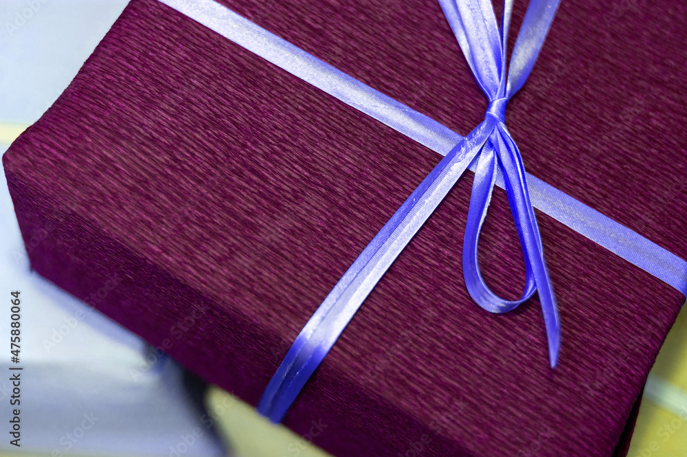 A purple gift box tied with a blue ribbon. Present for christmas, new year or birthday.