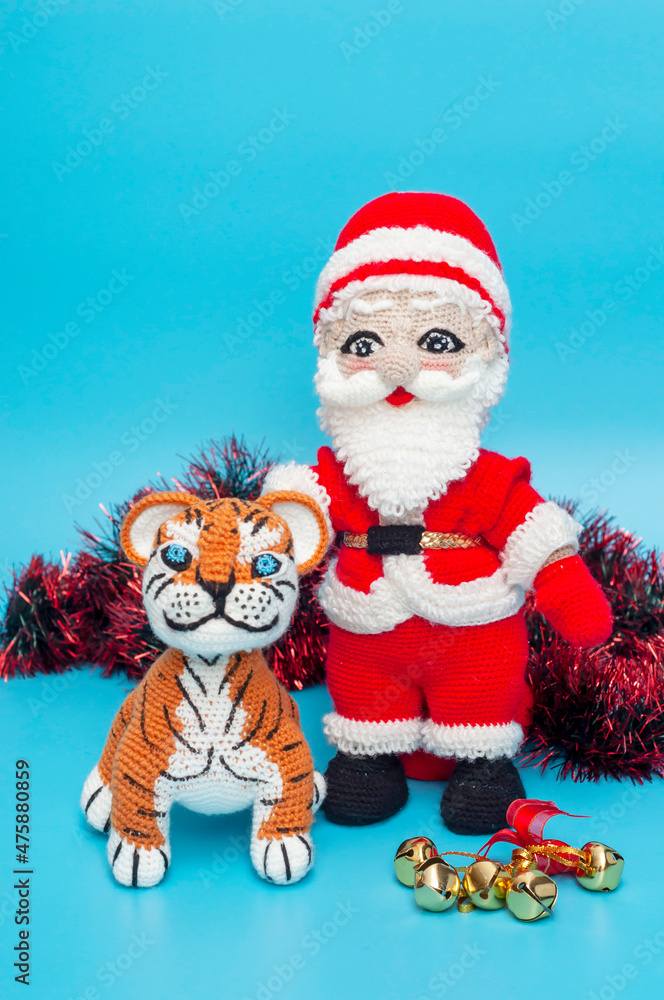 On a blue background there are knitted toys of Santa Claus and a tiger next to tinsel and a Christmas tree toy. vertical snapshot. On a blue background there are knitted toys of Santa Claus and a tiger next to tinsel and a Christmas tree toy. vertical snapshot.