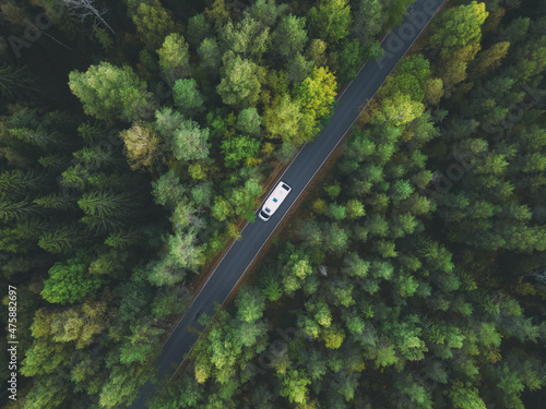 Fotografia White camper van with solar panels drive through green forest