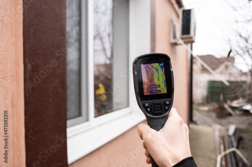 A male hand holds a thermal imager at the window of a house. Search for heat loss in private houses.