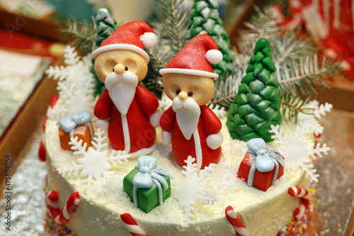 Creamy cake with Santa Claus figures and sweet Christmas decorations in store window. Confectionery, dessert for New year celebration