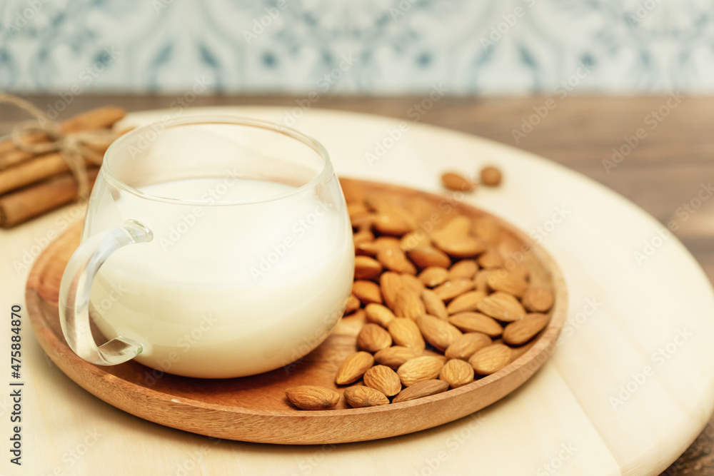 Non diary milk. Vegan food composition with cup of almond milk and almond nuts on a wooden plate and cinnamon sticks on a eco friendly kitchen. Rustic still life with vegan healthy product Non diary milk. Vegan food composition with cup of almond milk and almond nuts on a wooden plate and cinnamon sticks on a eco friendly kitchen. Rustic still life with vegan healthy product