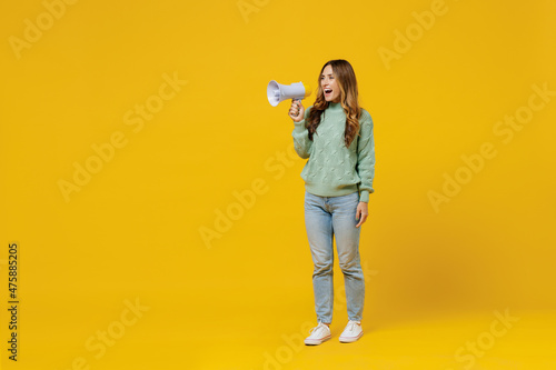 Full body young woman 30s wearing green knitted sweater hold scream in megaphone announces discounts sale Hurry up isolated on plain yellow color background studio portrait. People lifestyle concept.