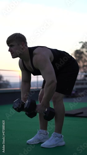 Caucasian white muscular man lifting dumbbells against the sunset sky background. Concept of willpower, motivation and passion. 4k vertical shot 