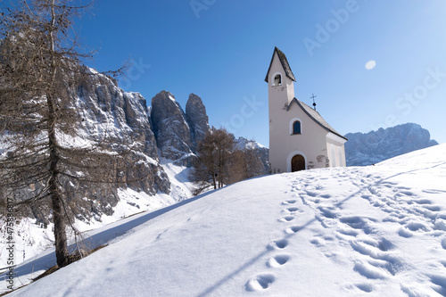 Chiesetta innevata a Passo Gardena sulle Dolomiti in inverno, chiesetta stile alpino ai piedi delle vette del Gruppo Sella sulle Alpi Italiane