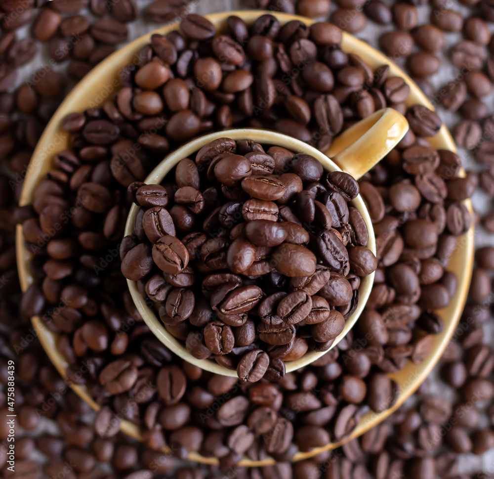 A cup filled with coffee beans surrounded by coffee beans. Cutting board, recipe, advertisement, catalog, menu, website, poster, postcard. Coffee beans close up. Dried and roasted coffee beans.