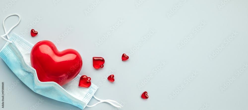 Red heart with medical protection mask on light blue background, top view, copy space. Concept of healthcare, self-defense.