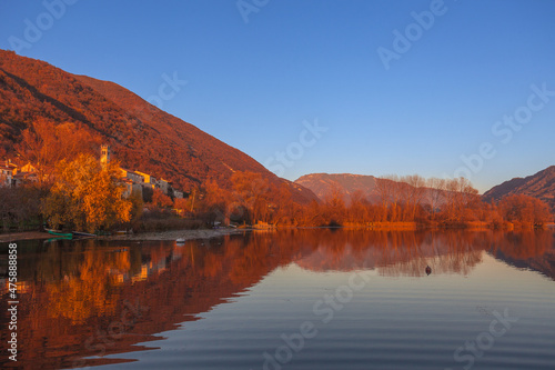 Autumn sunset on a small village of Santa Maria on the shore of a lake surrounded by colorful woods. Revine Lakes, Veneto, Italy. Concept about reflection and relaxation