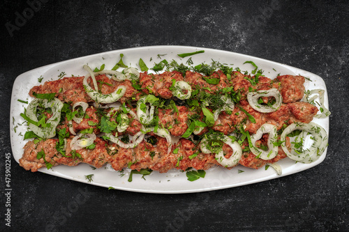 LULYA-KEBAB with herbs and onions on a plate, on a dark background