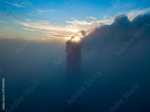 High chimney of a thermal power plant above the fog in the rays of the sunset. Aerial drone view.