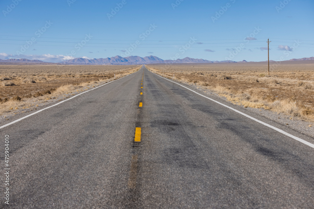 Lonely asphalt road stretches into the middle of nowhere in the desert lined by power poles Lonely asphalt road stretches into the middle of nowhere in the desert lined by power poles