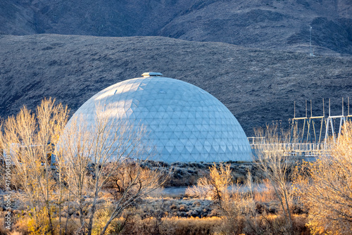 Dome and structures of a power plant seen through bushes and trees across the desert