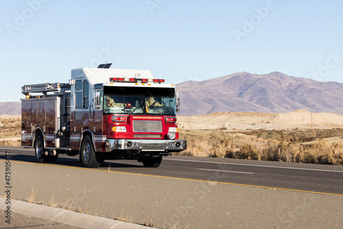 Red and white fire truck driving down a road in the desert responding to an emergency call