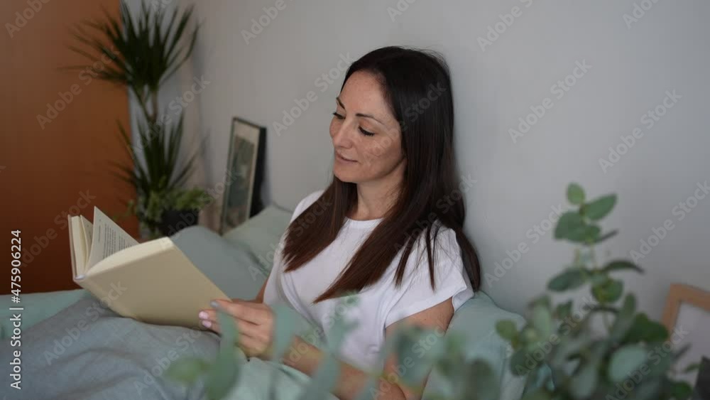 Beautiful relaxed woman reading in bed in bedroom decorated with plants. Slowdown concept Beautiful relaxed woman reading in bed in bedroom decorated with plants. Slowdown concept