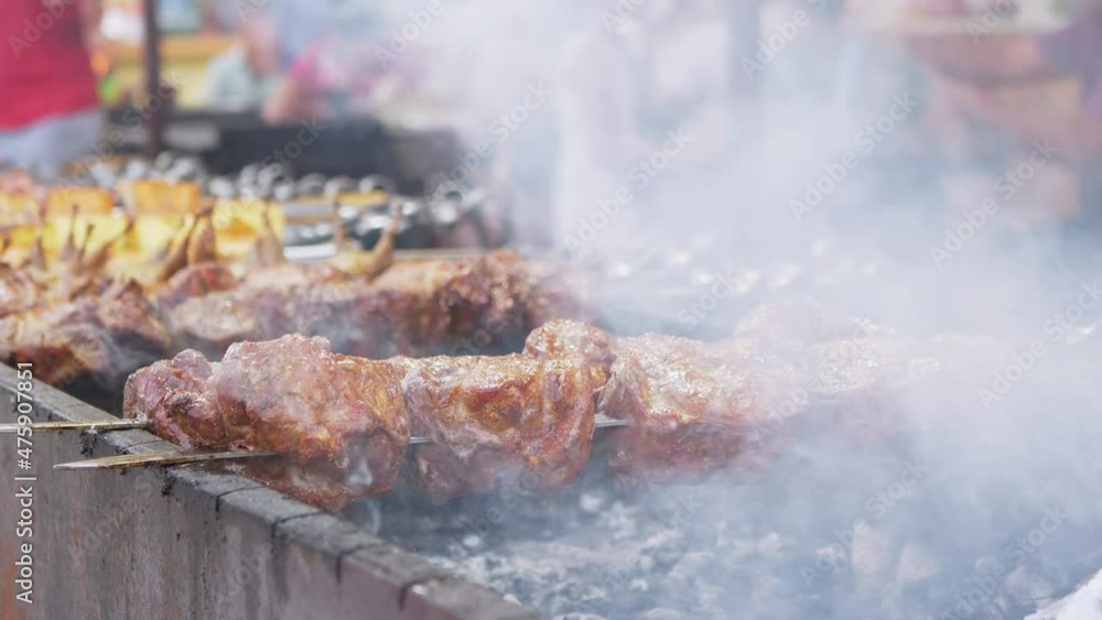Grilling Juicy Shish kebab outdoors. Barbecue, grilled meat on a charcoal grill in smoke. Chef rotates the fried pork on a skewer. Street Food trade. Lots of hungry people tourist on festival. 4K. Grilling Juicy Shish kebab outdoors. Barbecue, grilled meat on a charcoal grill in smoke. Chef rotates the fried pork on a skewer. Street Food trade. Lots of hungry people tourist on festival. 4K.