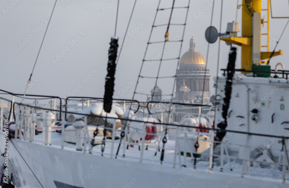 Fototapeta premium The golden dome of Isaac cathedral through old moored sail boat at frosty day, Winter landscape of St. Petersburg