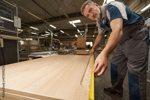 Concentrated male carpenter measuring the length of plank