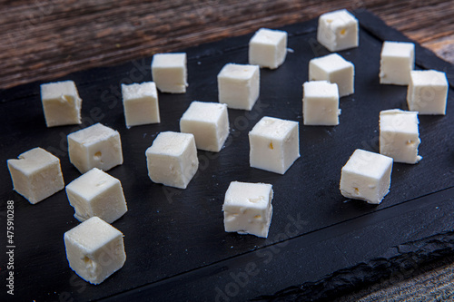 Feta Cheese Cubes on wooden cutting board. Square cubes of feta cheese isolated on wood board with knife.