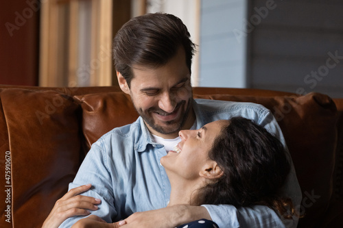 Head shot happy affectionate millennial bearded man cuddling beautiful wife, enjoying sweet tender weekend time together at home, talking speaking discussing life news, joking or dreaming indoors.